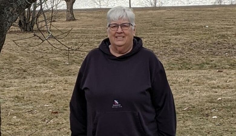 A woman stands up in a field next to a tree.