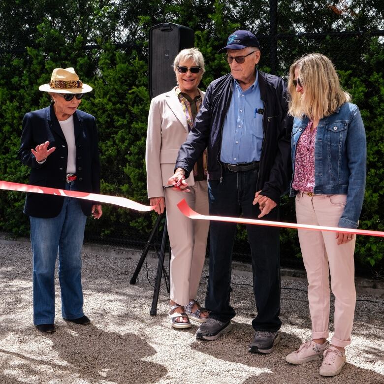 Four people stand as one man cuts a red ribbon. 