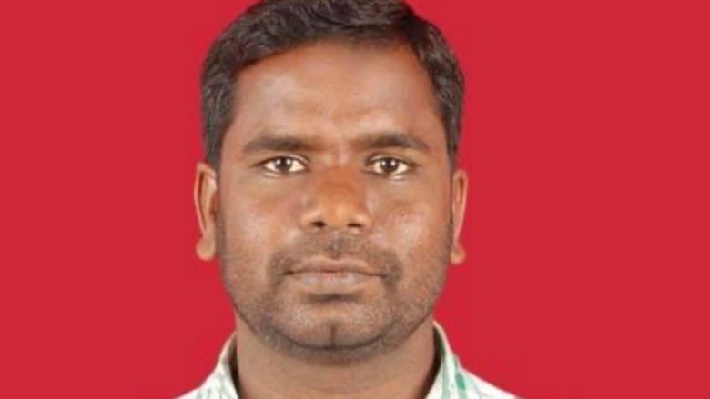 A man stands in front of a red background.