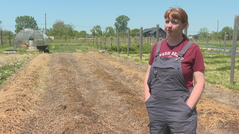 A woman in overalls tands in front of a small field 