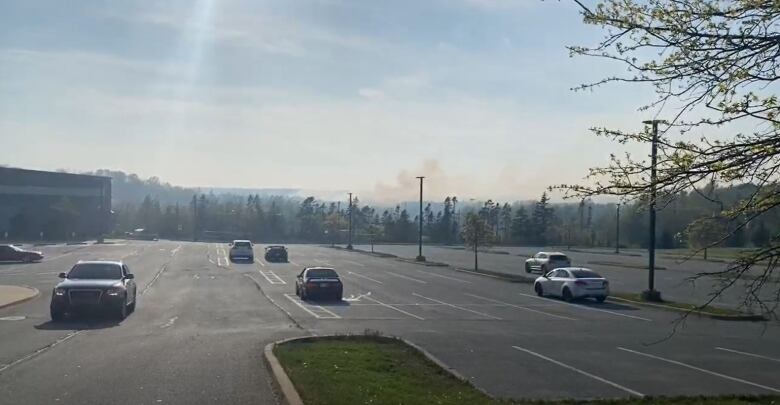 Cars in a parking lot with smoke in the distance.