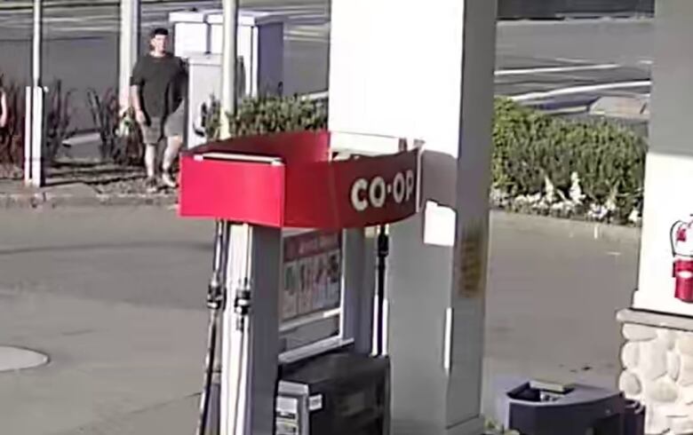 A surveillance camera still of a man wearing a black T-shirt at a gas station.