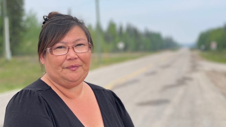 Woman in black shirt and glasses stands on rural road.