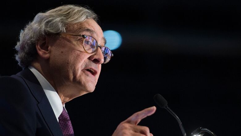 Grey haired man speaks into microphone, profile shot.