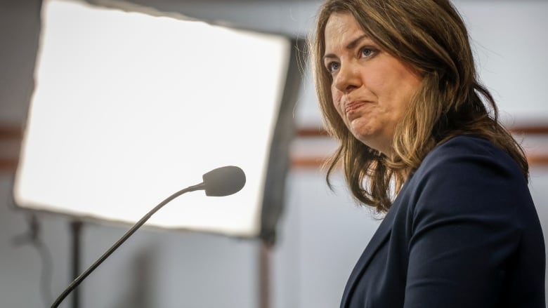 A politician listens before speaking into a microphone during a news conference 