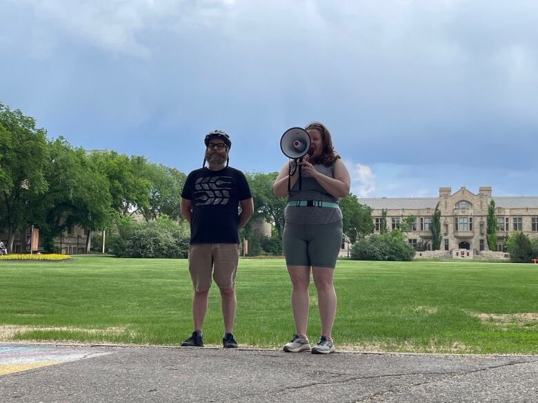 A man in a bicycle helmut stands beside a woman with a bullhorn. 