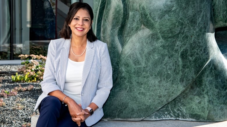 A woman in a light blue and white blazer is seated for a photo.