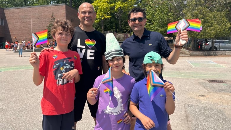 David Toto, back row left, and Laurent Papaix, back row right, and their three children wave Progress Pride flags at a special celebration at St. Denis Catholic School on Wednesday in Toronto.