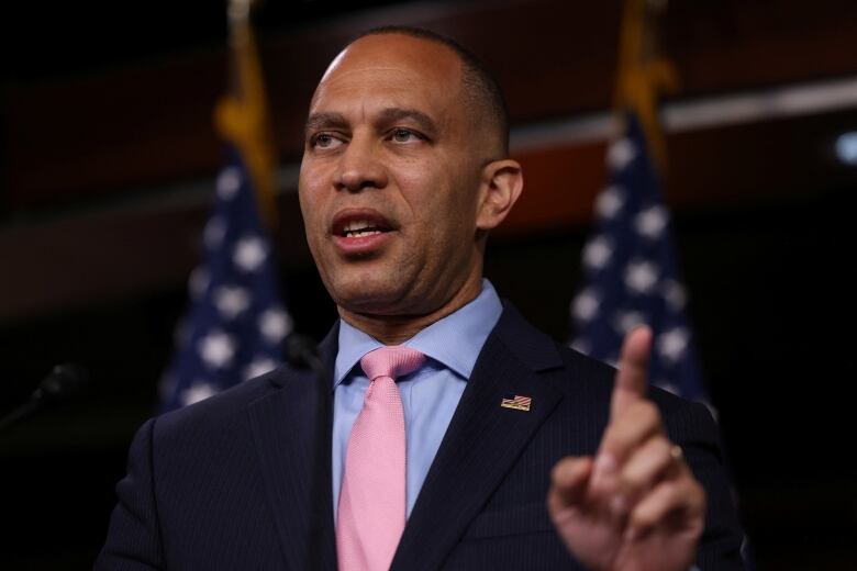 A man in suit and tie raises an index finger as he speaks.