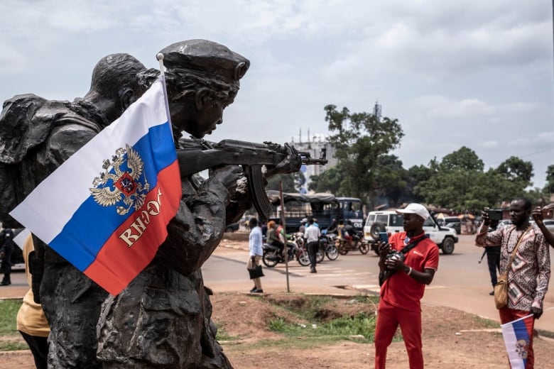 People stand to the right of a statue with a Russian flag on it. 