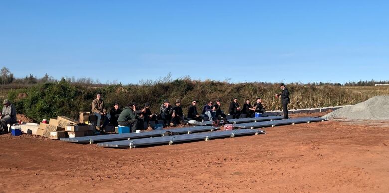 15 people sit on a bench during a workbreak.