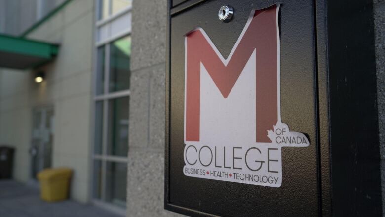 A sticker for M College of Canada is stuck to a mailbox outside of the non-subsidized private college. 