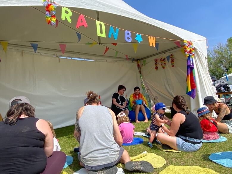 A few parents and their children sit outside the Rainbow Tent as two performers inside speak with them