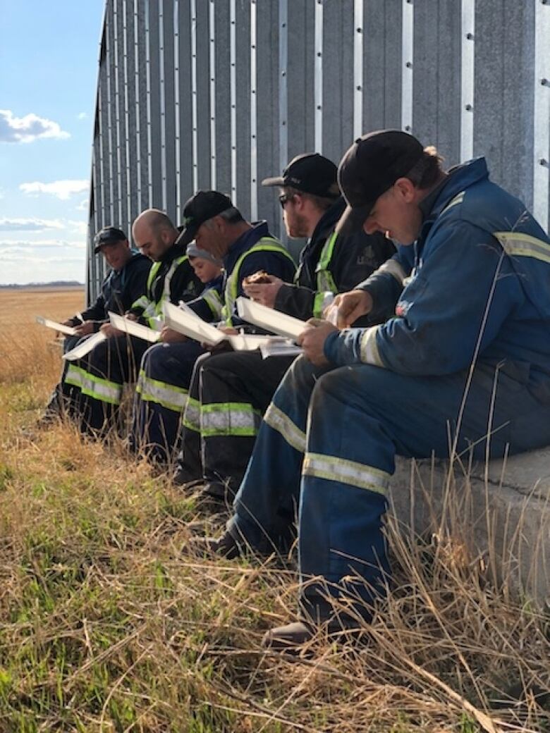 Five men and a boy sit eating lunch while wearing work clothes.