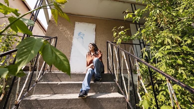 Woman sits on the front steps of a boarded-up house.