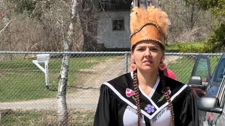 A woman with two long braids wears a graduation gown and a brown headdress. 