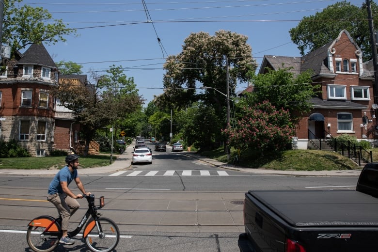 A male cyclist rides by two multiplex buildings on opposite corners of a T-intersection.