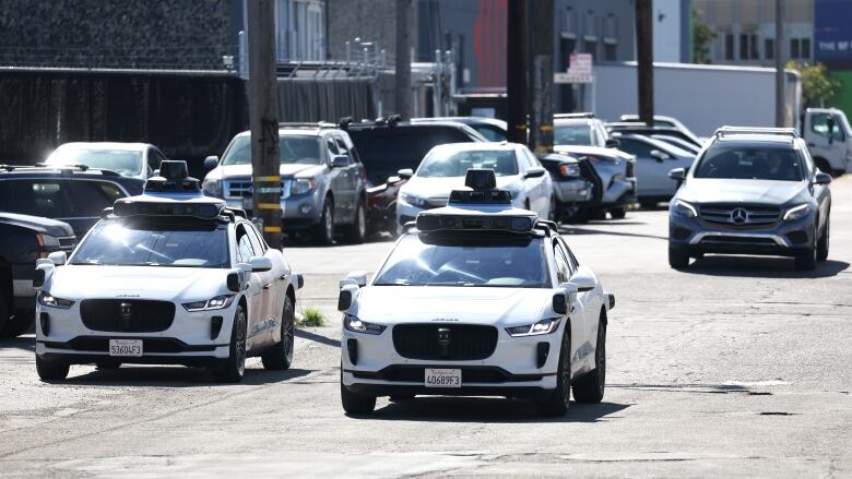 Three cars, including two self-driving models, share a road in traffic.