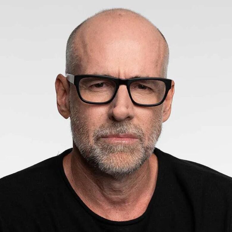 A bald man with a gray beard wears dark glasses with a thick frame.