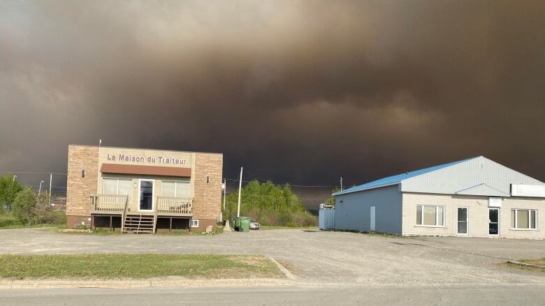 A thick cloud of dark brown smoke hangs over two buildings.