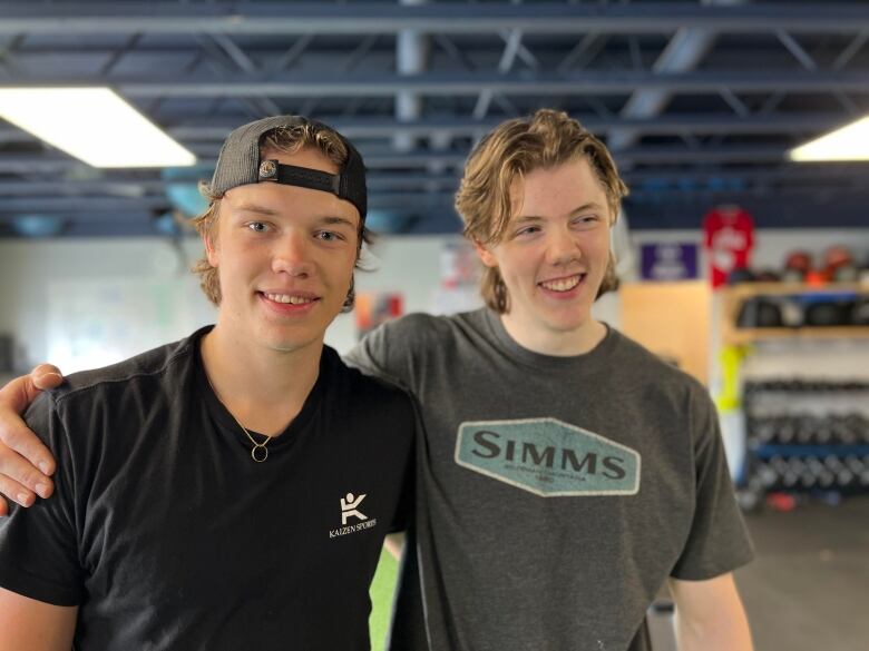 Two guys with their arms around each other smile.