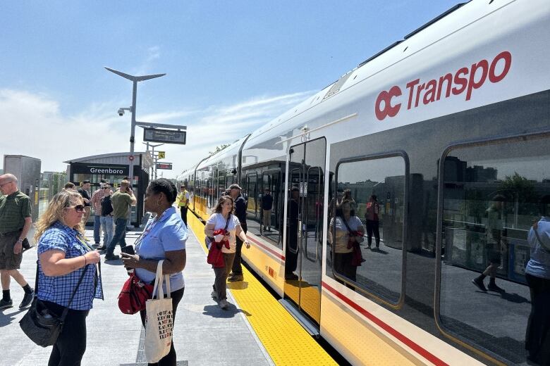 People walk by a stopped red and white public transit train on a late spring morning.