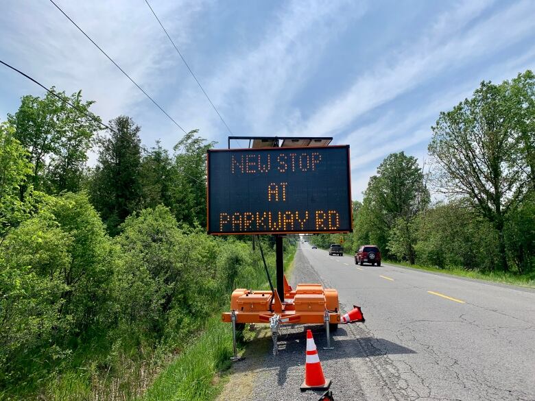 A large electric traffic sign sits on a rural road and reads 