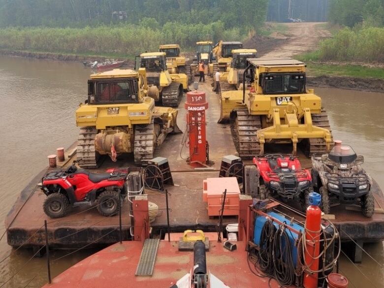 Bulldozers and ATVs on a ferry on a body of water.