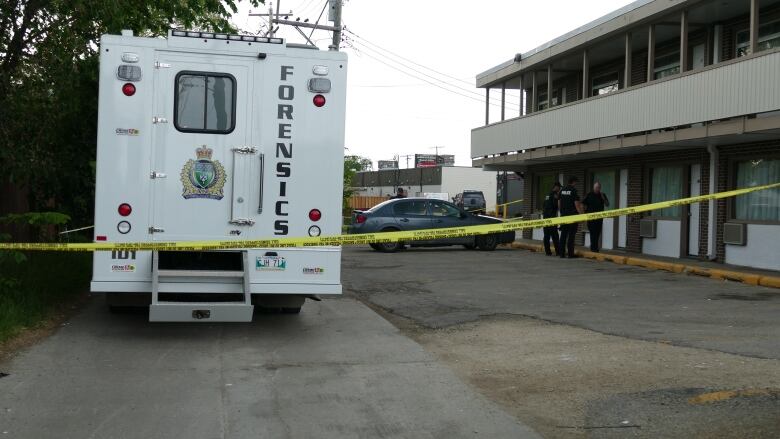 A forensics van is parked at a motel parking lot behind yellow tape.