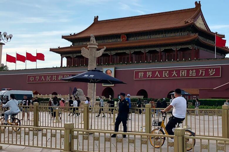 A security guard watches as cyclists and pedestrians pass by outside Tiananmen Square in Beijing. 