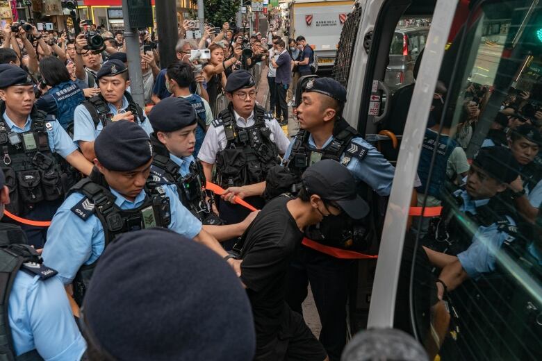 A handcuffed person is led into a van by police officers.