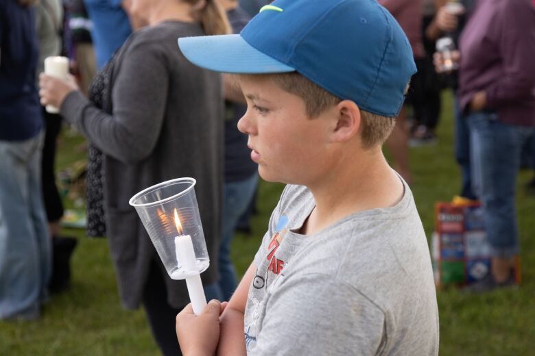 A child carries a candle in a plastic cup at a vigil.