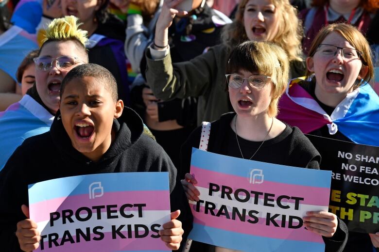 Teenaged kids hold pink and blue striped signs that say 