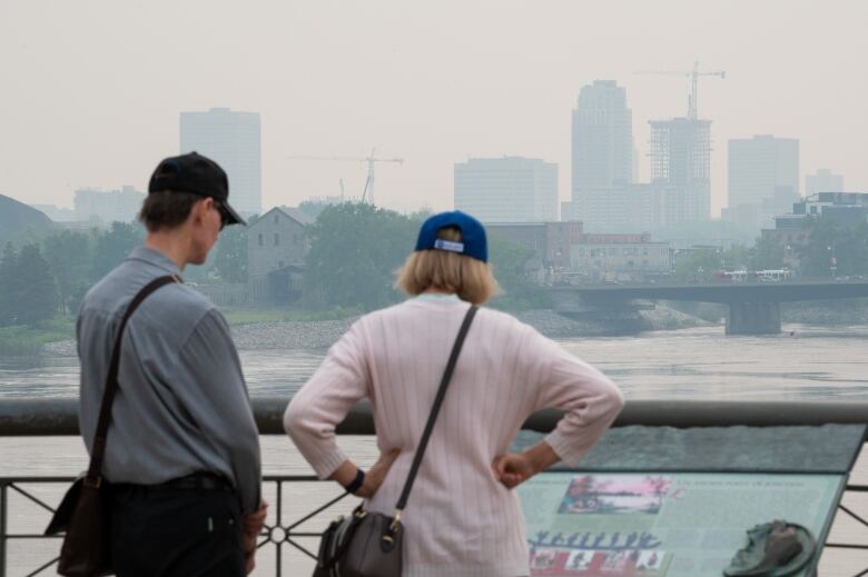 Two people look at an information board on a very hazy day in a city.