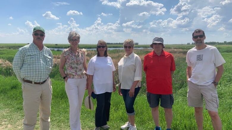 A group of people stand in front of a wetland in the sun. 