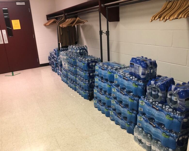 About 27 pallets of plastic water bottles are stacked underneath a clothing hanger rode.