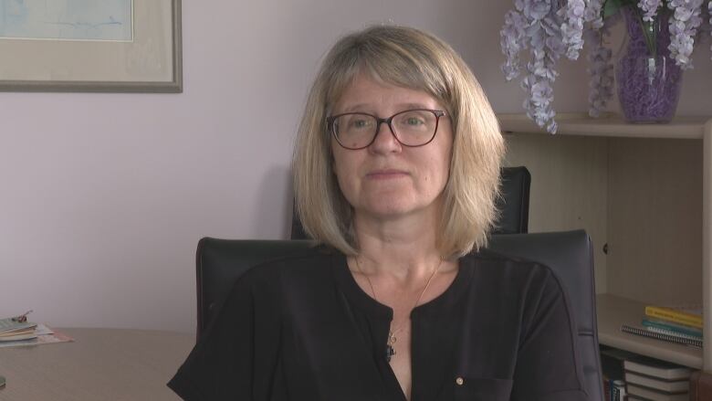 A woman in a black shirt sits in a purple room. 