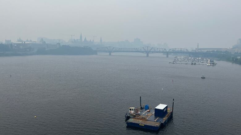 Smoke hangs over the skyline of two cities and the river between them.