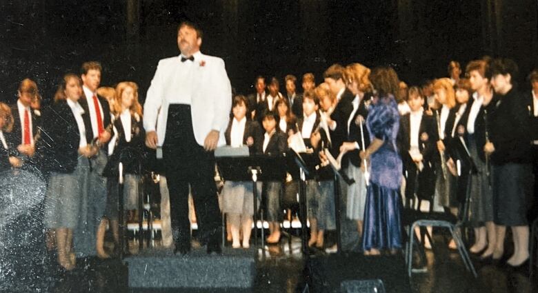 band leader stands on speaker in front of students gathered on stage