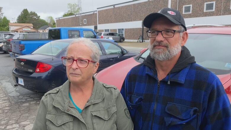 A woman and a man standing in a parking lot looking off camera.