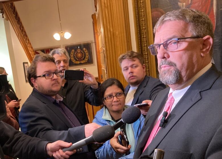 A crowd of people surrounding a man and holding microphones up to him.