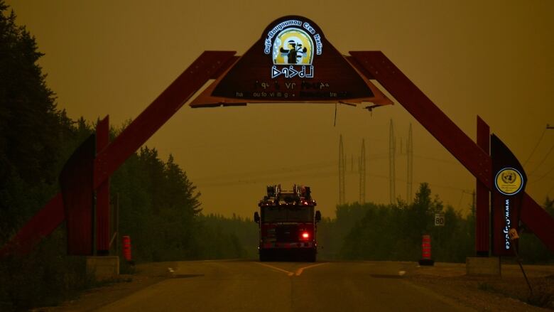 A fire truck surrounded by an orange, smoke filled sky at dusk drives on a gravel road. 