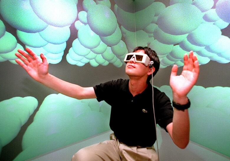 A man wearing 3D glasses extends his arms in a room painted with images of molecules.