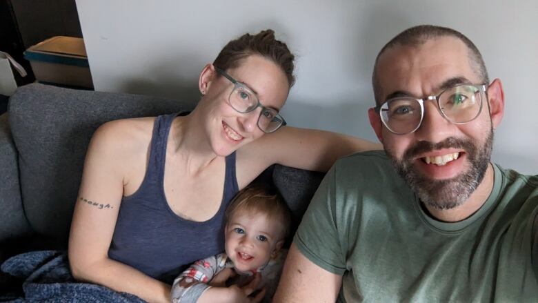 A man sits on a sofa with a woman and a baby smiling in between them. 