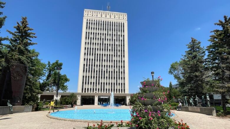 A picture of a tall blocky building with a fountain in front as well as a plant feature. 