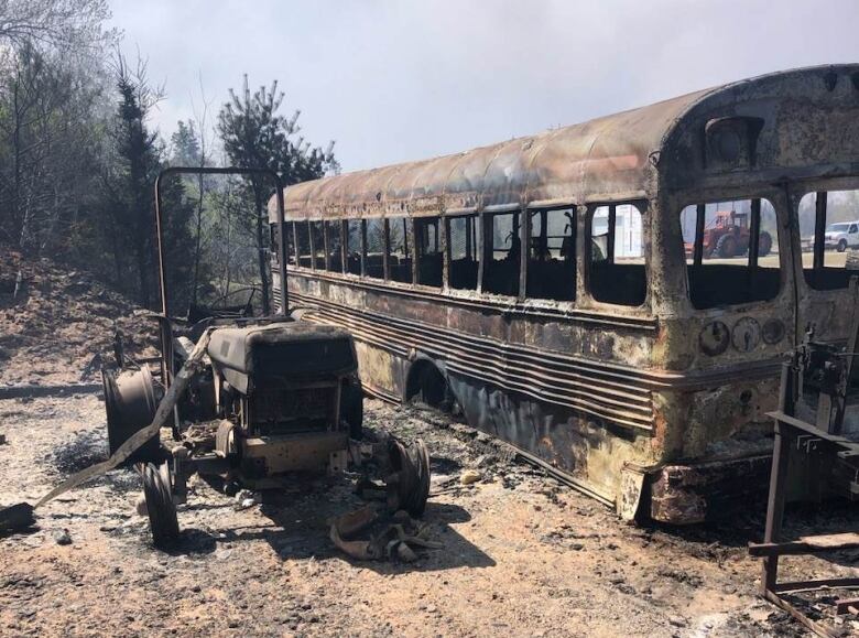 A burned out school bus and tractor in a farmer's field.