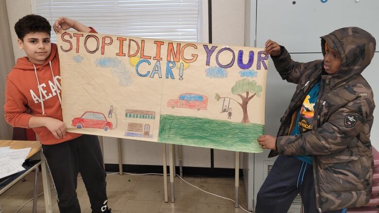 Two kids hold up a large hand-drawn poster that says 