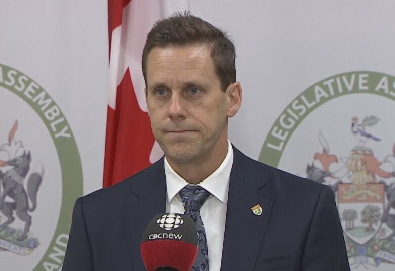 Man in business suit stands at CBC microphone. 