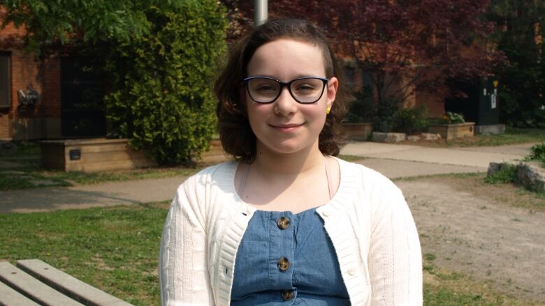 A kid wearing glasses and a white cardigan smiles at the camera.