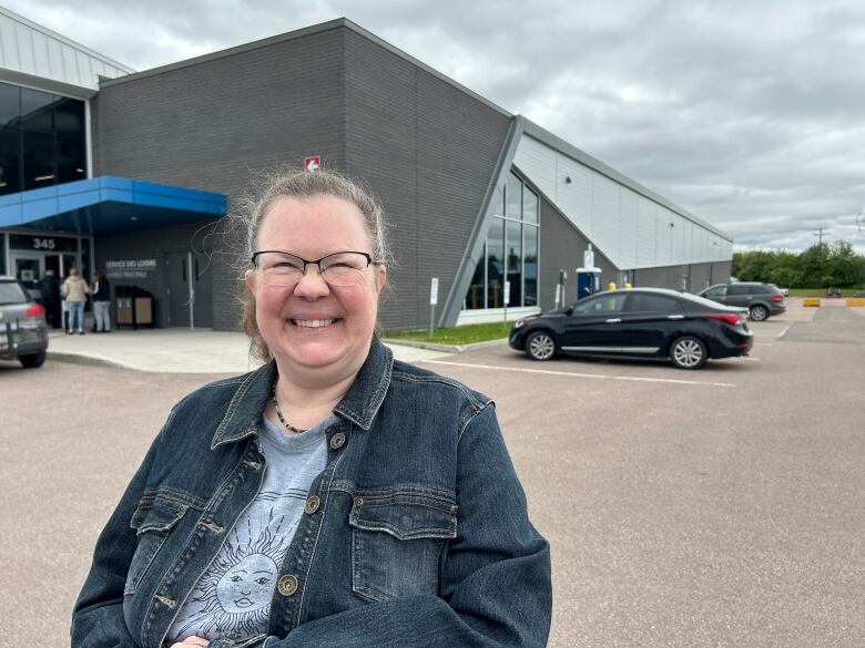 A smiling woman in a jean jacket in a parking lot.